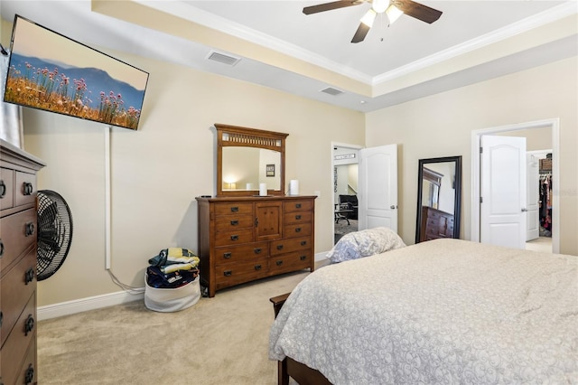 bedroom with a spacious closet, ceiling fan, a tray ceiling, light colored carpet, and ornamental molding