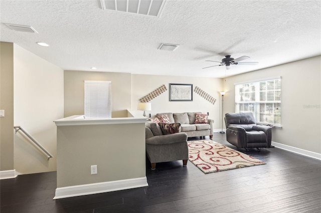 living room with a textured ceiling, dark wood-type flooring, and ceiling fan