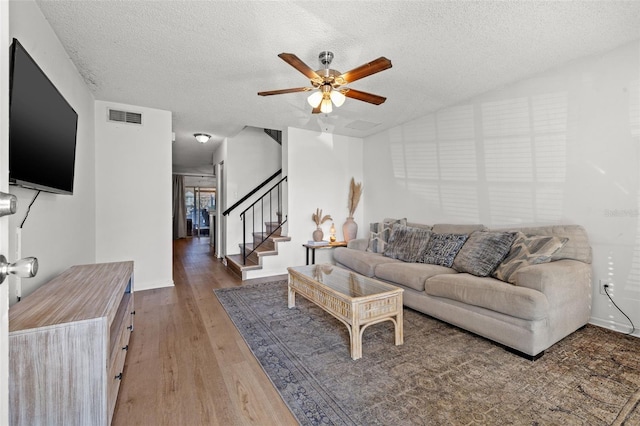 living room with a textured ceiling, ceiling fan, and dark wood-type flooring