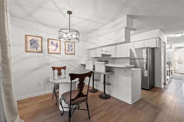 kitchen featuring kitchen peninsula, stainless steel fridge, white cabinets, hardwood / wood-style floors, and hanging light fixtures