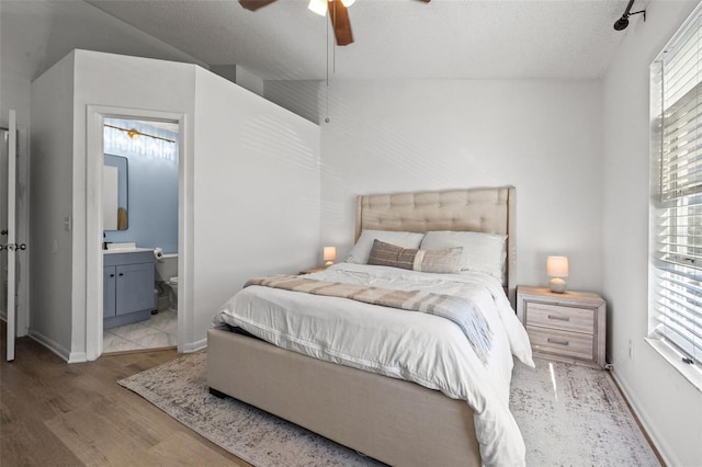 bedroom featuring lofted ceiling, ensuite bath, ceiling fan, light wood-type flooring, and a textured ceiling