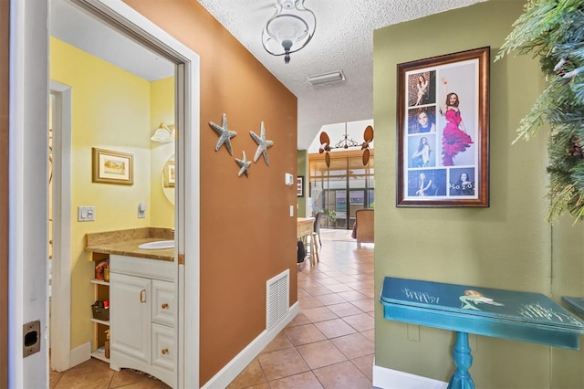 hall featuring sink, light tile patterned floors, and a textured ceiling