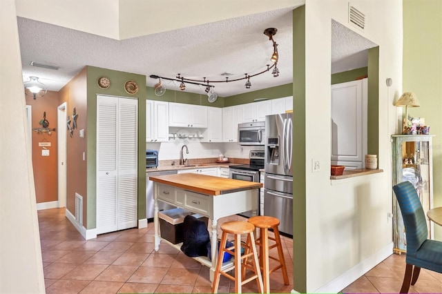 kitchen with wood counters, a textured ceiling, stainless steel appliances, sink, and white cabinets