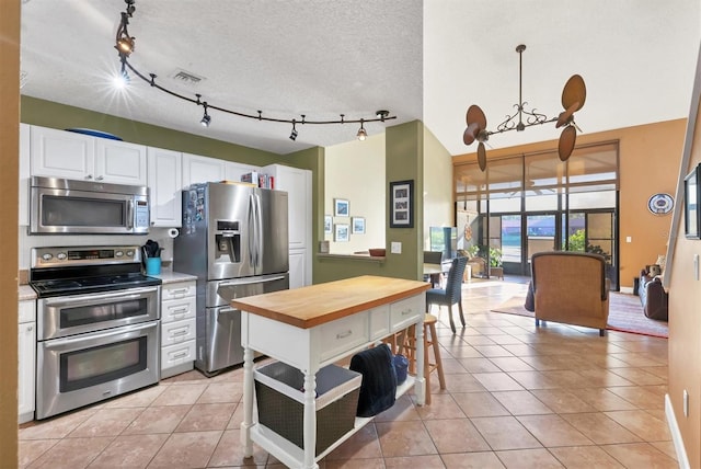 kitchen with wooden counters, hanging light fixtures, light tile patterned flooring, white cabinetry, and stainless steel appliances