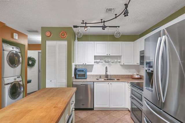 kitchen with stacked washer / dryer, white cabinetry, sink, and appliances with stainless steel finishes