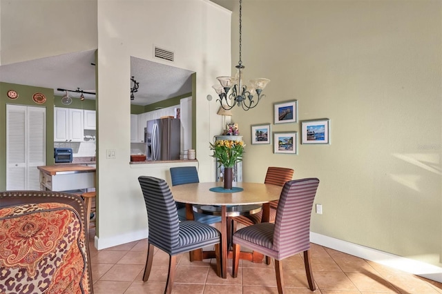 tiled dining area with a chandelier, a textured ceiling, and rail lighting