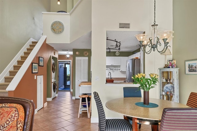 dining space with tile patterned flooring, stacked washing maching and dryer, a high ceiling, and an inviting chandelier