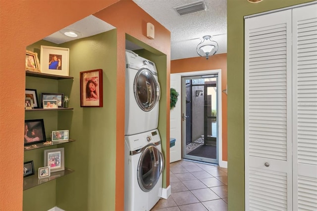 laundry room featuring stacked washer / dryer, light tile patterned floors, and a textured ceiling