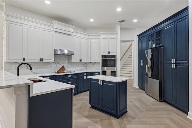 kitchen with blue cabinetry, white cabinetry, a kitchen island, exhaust hood, and appliances with stainless steel finishes