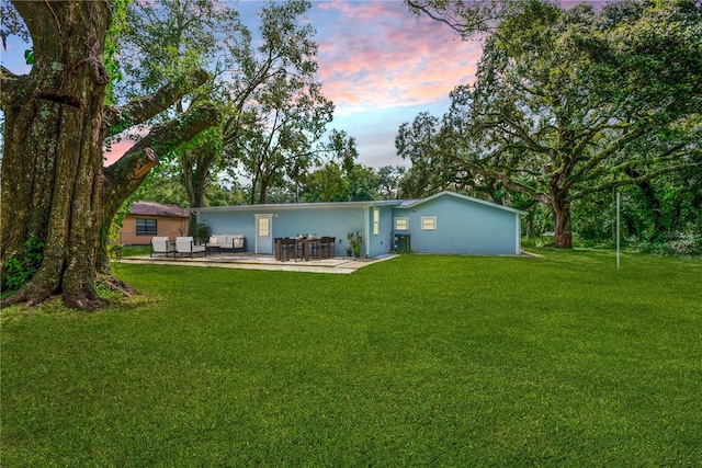 back house at dusk with a lawn, central AC unit, and a patio area