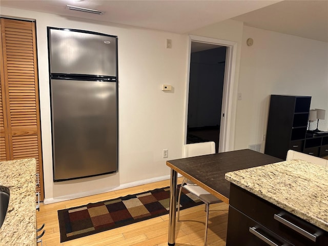 kitchen with light stone countertops, light wood-type flooring, and stainless steel refrigerator