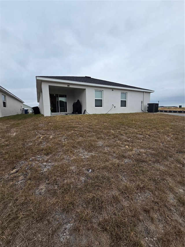 rear view of house with central AC unit and a lawn