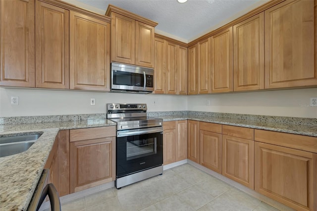 kitchen with appliances with stainless steel finishes, a textured ceiling, light stone counters, and light tile patterned floors