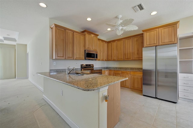 kitchen featuring kitchen peninsula, appliances with stainless steel finishes, light stone counters, ceiling fan, and sink