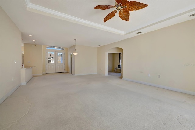 empty room with a raised ceiling, light carpet, french doors, and ceiling fan