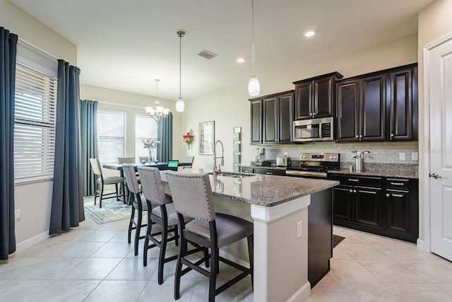 kitchen with a kitchen island with sink, a kitchen breakfast bar, sink, hanging light fixtures, and stainless steel appliances