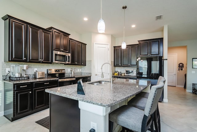 kitchen featuring pendant lighting, sink, light stone countertops, an island with sink, and stainless steel appliances