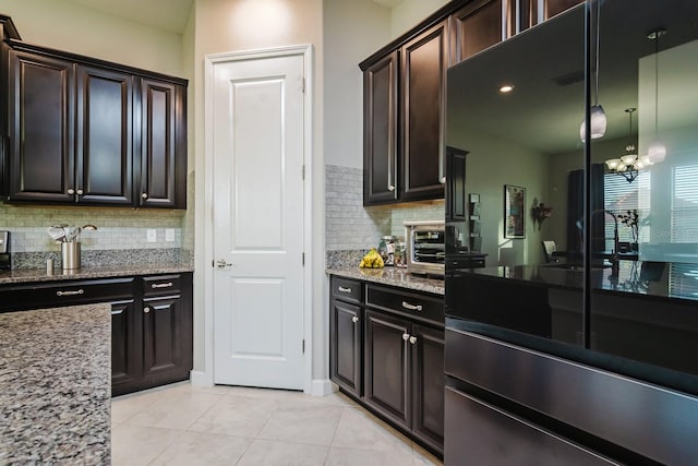 kitchen with an inviting chandelier, tasteful backsplash, light stone counters, pendant lighting, and light tile patterned floors