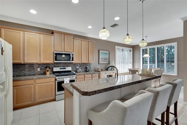 kitchen with light brown cabinets, stainless steel appliances, hanging light fixtures, and an island with sink