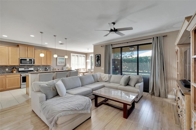 living room with a wealth of natural light, crown molding, ceiling fan, and light wood-type flooring