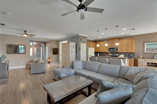 living room with ceiling fan with notable chandelier, light hardwood / wood-style flooring, and ornamental molding