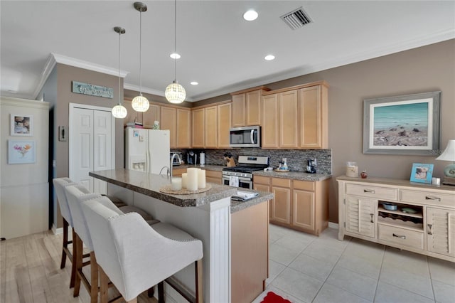 kitchen with light brown cabinetry, ornamental molding, stainless steel appliances, hanging light fixtures, and an island with sink