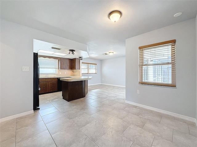 kitchen featuring light tile patterned flooring, black refrigerator, sink, a kitchen island, and dark brown cabinetry