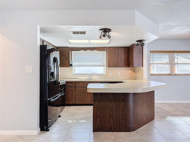 kitchen featuring kitchen peninsula, light tile patterned floors, black fridge, and dark brown cabinets