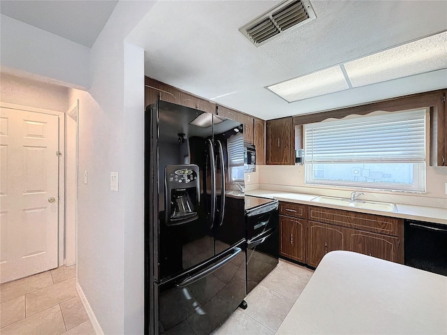 kitchen featuring black appliances, dark brown cabinetry, sink, and light tile patterned floors