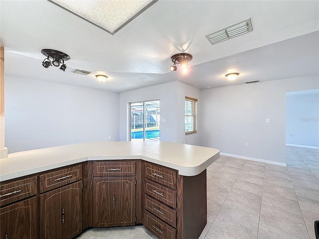 kitchen with kitchen peninsula, light tile patterned floors, dark brown cabinetry, and a textured ceiling