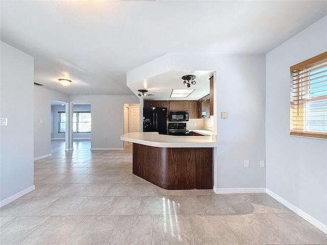 kitchen featuring kitchen peninsula, light tile patterned floors, a kitchen bar, and black appliances