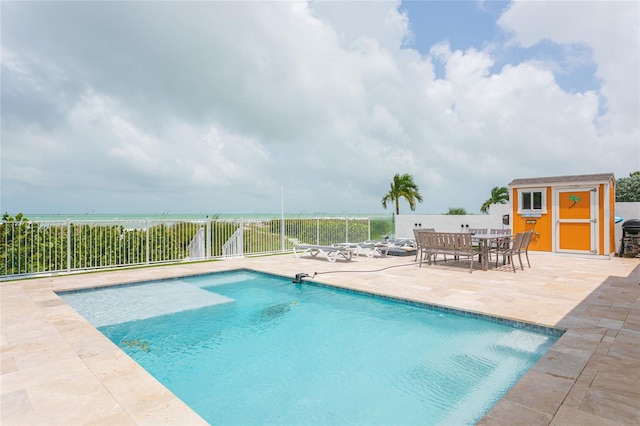 view of swimming pool with a patio area, a water view, and a storage unit