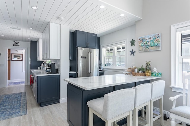 kitchen with kitchen peninsula, a kitchen breakfast bar, high end fridge, blue cabinetry, and light hardwood / wood-style flooring