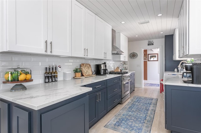 kitchen with white cabinets, light stone counters, wall chimney range hood, and high end stainless steel range oven