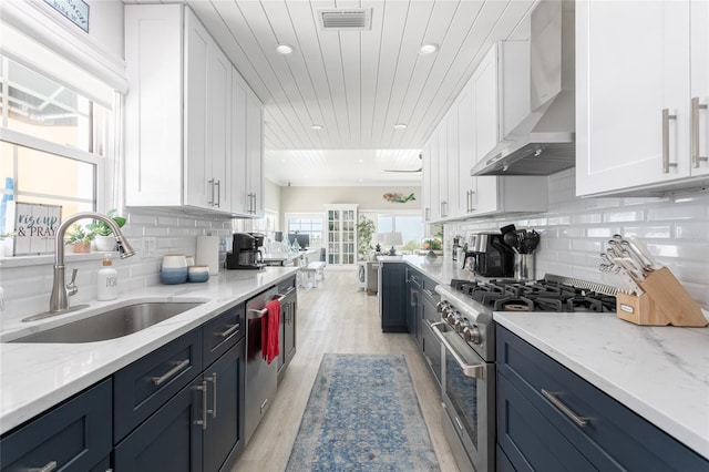 kitchen featuring white cabinetry, stainless steel appliances, and wall chimney range hood