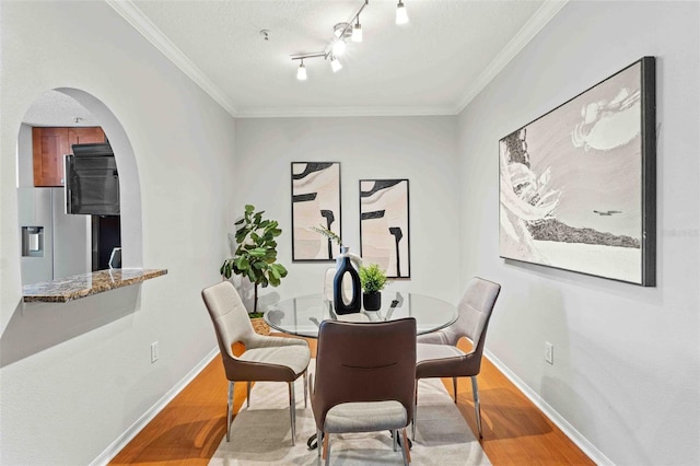 dining space featuring a textured ceiling, light wood-type flooring, and crown molding