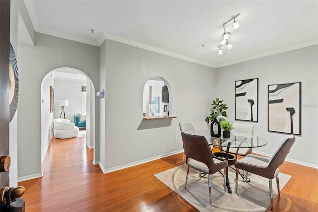 dining space featuring a textured ceiling, crown molding, light hardwood / wood-style floors, and track lighting