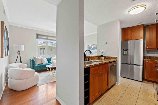 kitchen featuring dark stone counters, sink, light tile patterned floors, ornamental molding, and appliances with stainless steel finishes