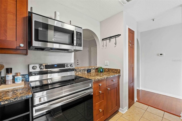 kitchen with light tile patterned floors, a textured ceiling, stainless steel appliances, and dark stone countertops