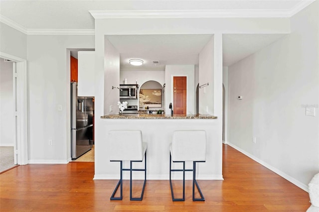 kitchen featuring kitchen peninsula, stainless steel appliances, crown molding, stone countertops, and a breakfast bar area