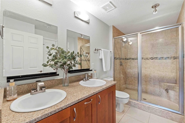 bathroom featuring tile patterned flooring, a textured ceiling, toilet, vanity, and a shower with shower door