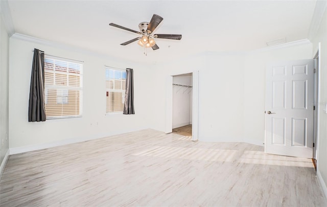 unfurnished bedroom featuring crown molding, ceiling fan, a spacious closet, light wood-type flooring, and a closet