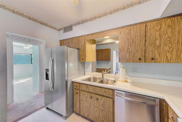 kitchen featuring appliances with stainless steel finishes, a textured ceiling, light colored carpet, and sink