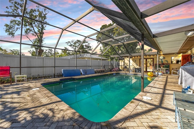 pool at dusk featuring a patio and a lanai