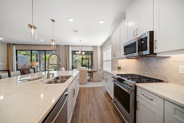 kitchen featuring sink, white cabinetry, light stone counters, wood-type flooring, and stainless steel appliances