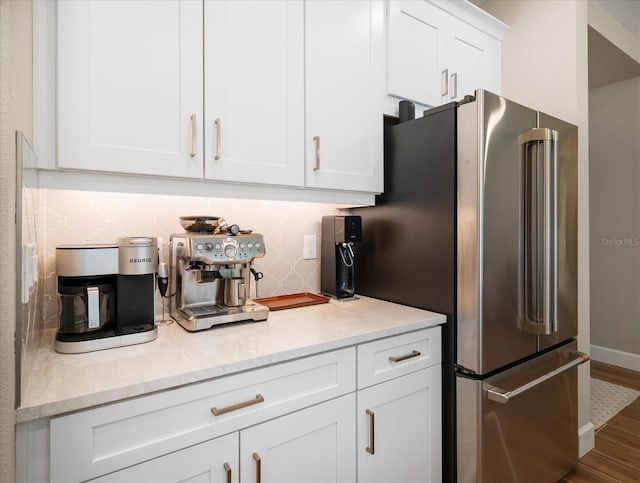 kitchen featuring decorative backsplash, light stone counters, high end fridge, hardwood / wood-style floors, and white cabinetry