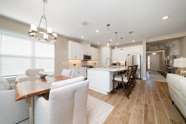 kitchen featuring white cabinetry, decorative light fixtures, a kitchen island with sink, appliances with stainless steel finishes, and light wood-type flooring