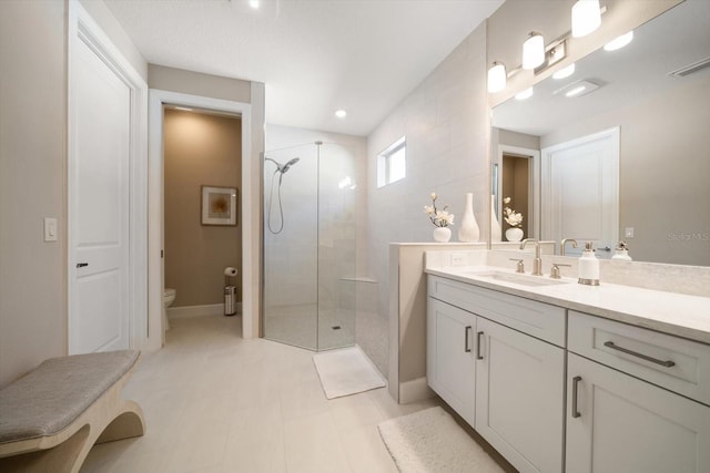 bathroom featuring tile patterned flooring, vanity, toilet, and a tile shower