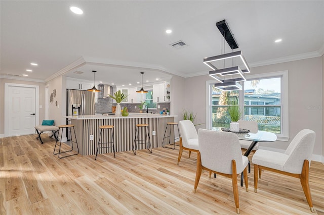 dining area featuring crown molding, sink, and light hardwood / wood-style flooring