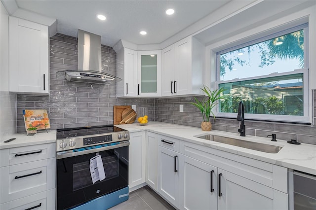 kitchen with electric stove, wall chimney range hood, sink, and white cabinets